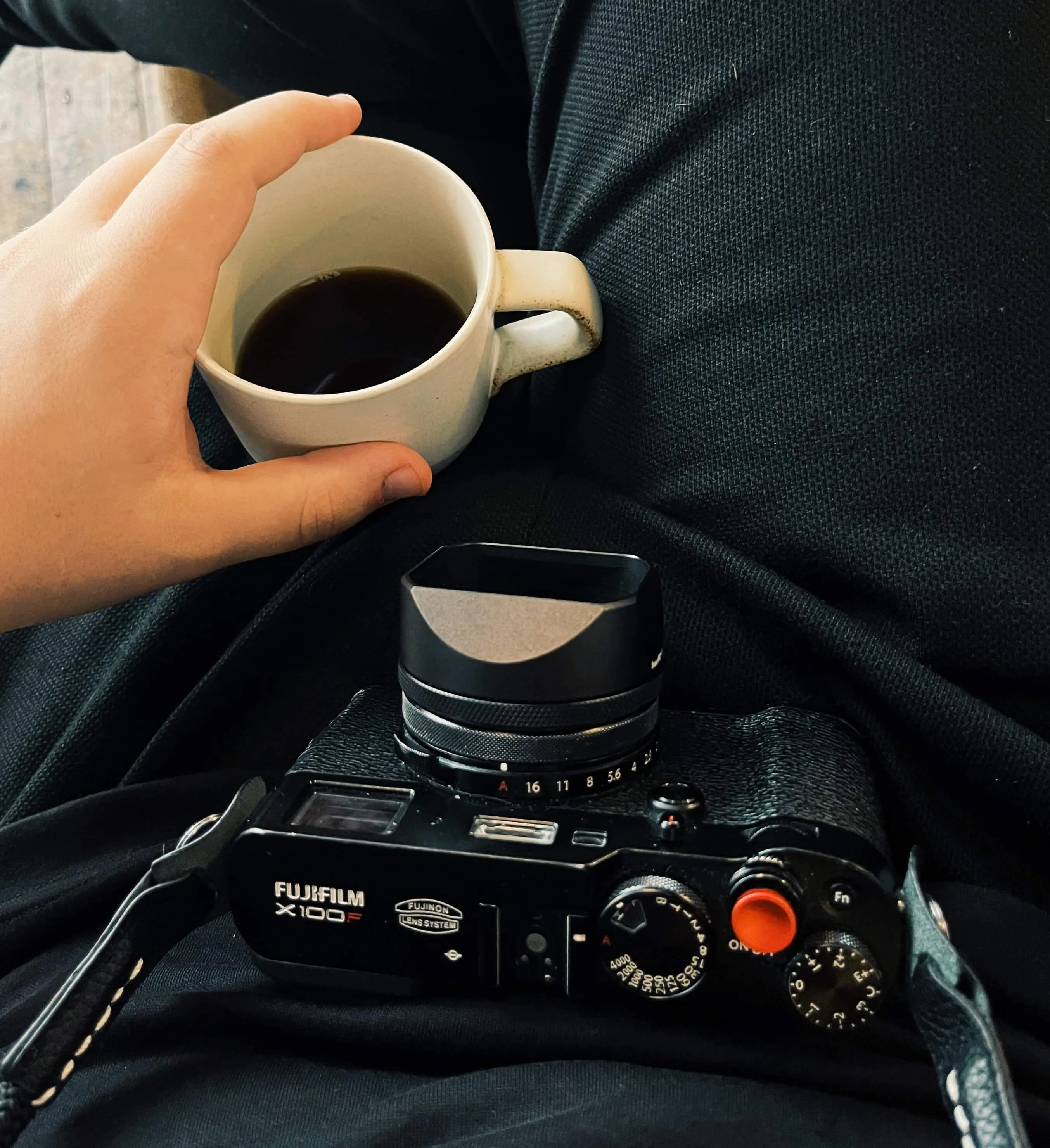 Camera on the lap and the picture taker holding a cup of coffee