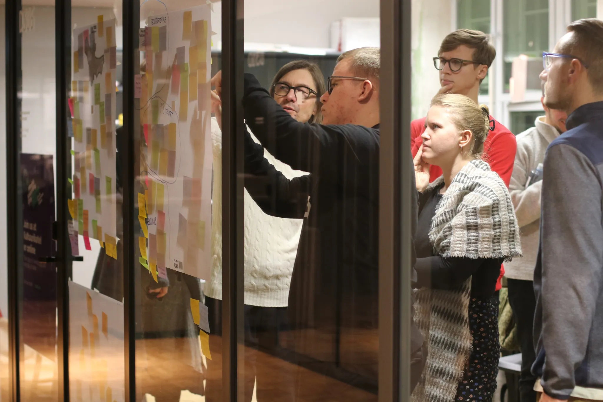 IxD.ma students behind a glass wall putting post-its on paper.